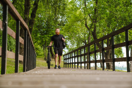 Adult handsome tattooed bearded smiling happy man in black sport suit looking aside, while walking...