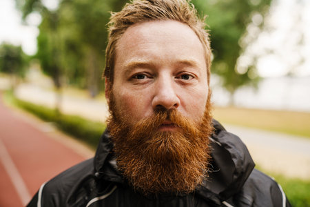 Ginger bearded sportsman looking at camera while working out in park outdoorsの写真素材