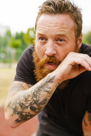 Ginger bearded sportsman resting while working out in park outdoorsの写真素材