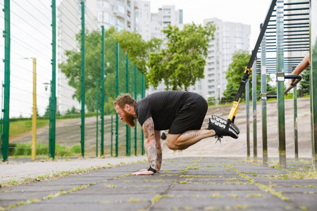 Ginger bearded sportsman doing exercise while working out on playground outdoorsの写真素材
