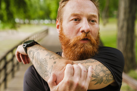 Ginger bearded sportsman doing exercise while working out in park outdoorsの写真素材