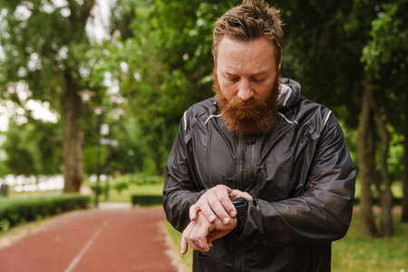 Ginger bearded sportsman using smartwatch while working out in park outdoorsの写真素材