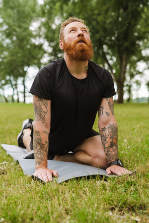 Ginger bearded man doing exercise during yoga practice in park outdoorsの写真素材