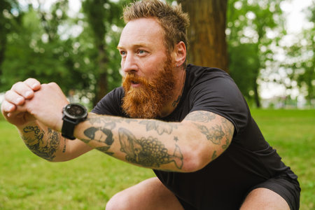 Ginger bearded man doing exercise during workout in park outdoorsの写真素材