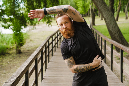 Ginger bearded sportsman doing exercise while working out in park outdoorsの写真素材