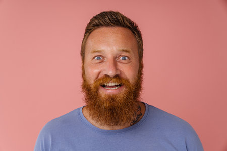 Ginger excited man with beard smiling and looking at camera isolated over pink backgroundの写真素材