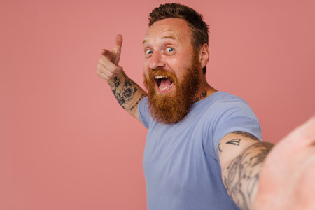Ginger excited man taking selfie photo and gesturing isolated over pink backgroundの写真素材