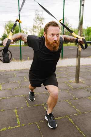 Ginger bearded sportsman doing exercise while working out on playground outdoors