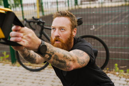 Ginger bearded sportsman doing exercise while working out on playground outdoors