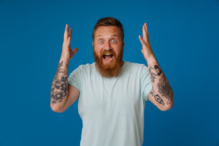 Ginger shocked man with beard expressing surprise at camera isolated over blue backgroundの写真素材