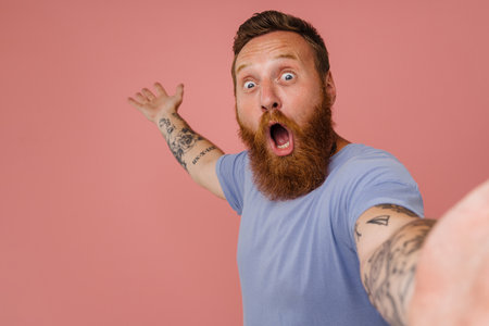 Ginger excited man taking selfie photo and gesturing isolated over pink backgroundの写真素材