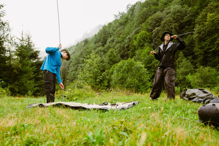 Young white people wearing trekking equipment putting up tent while hiking in mountain forest