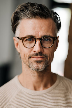 Closeup of white middle-aged man in eyeglasses looking at camera while standing indoors