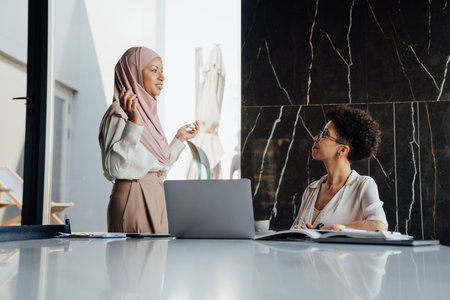 Middle-aged businesswoman and her female assistant talking together while working in officeの写真素材