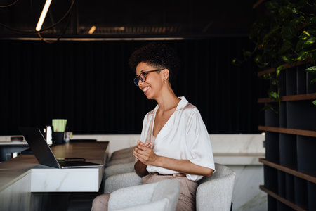 Middle-aged happy businesswoman using laptop while sitting in chair at cafeの写真素材