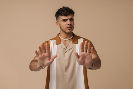 Young handsome serious frowning man doing rejection gesture with stretched palms and looking at camera, while standing over isolated brown backgroundの写真素材