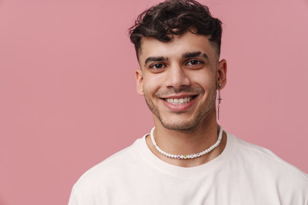 Young handsome stylish smiling man with piercing in necklace looking at camera , while standing over isolated pink backgroundの写真素材