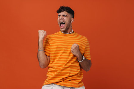 Brunette young man screaming while making winner gesture isolated over red backgroundの写真素材