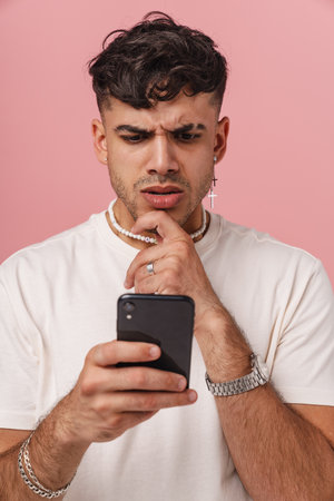 Young hadsome stylish thoughtful man looking at phone in his hand and touching his chin, while...