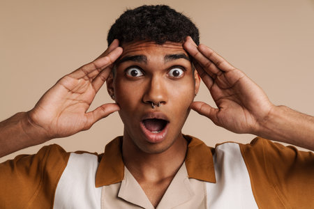 Young black man with piercing expressing surprise at camera isolated over beige backgroundの写真素材