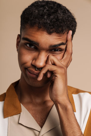 Young black man with piercing frowning while propping up his head isolated over beige background