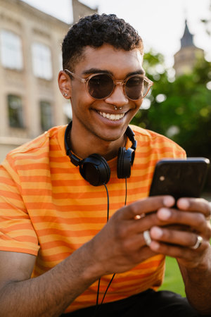 Young black brunette man wearing sunglasses using cellphone outdoorsの写真素材