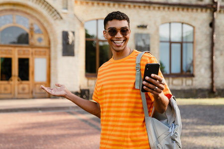 Young black brunette man wearing sunglasses walking outdoors with cellphoneの写真素材