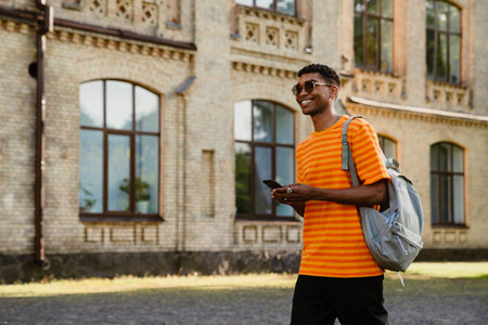 Young black brunette man wearing sunglasses walking outdoors with cellphone