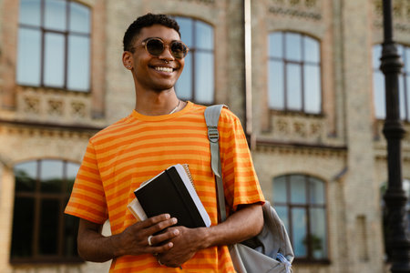 Young black brunette man wearing sunglasses holding notepad while walking outdoorsの写真素材