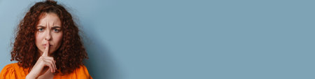 Displeased ginger young woman showing silence gesture isolated over blue background
