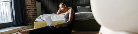 Healthy young fit african sportswoman using laptop computer while sitting on a fitness mat in the...