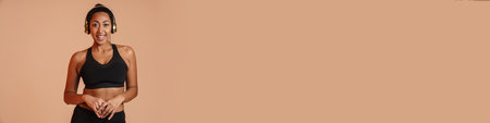Happy african american sportswoman posing in wireless headphones isolated over beige backgroundの写真素材