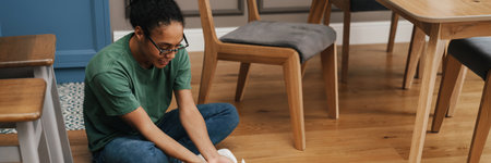 Smiling mid aged african woman playing with her dog in the kitchen, sitting on a floorの写真素材