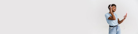 Laughing black woman listening music with headphones and cellphone isolated over white backgroundの写真素材