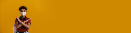 Young black woman in face mask showing stop gesture isolated over yellow backgroundの写真素材