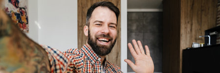 Portrait of a smiling man sitting on the floor and making selfie photo, waving hand