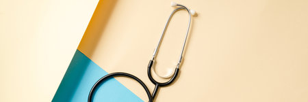 Overhead view of a stethoscope with a badge lying on a beige and blue background in the studio