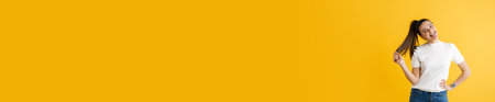 Young brunette woman making fun and showing her tongue isolated over yellow background