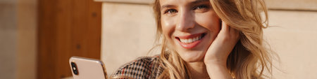 Smiling young blonde woman holding mobile phone while sitting on steps on a streetの写真素材