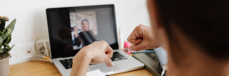 The rear view of female hands benting into fists while showing by video call to the laptop camera in the white roomの写真素材