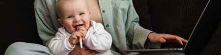 Happy mother with her baby working on laptop computer at home, croppedの写真素材