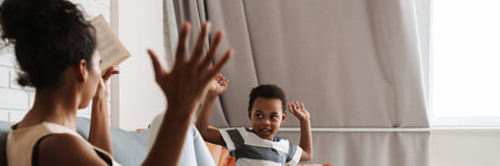 Black mother and son gesturing while sitting on sofa at homeの写真素材