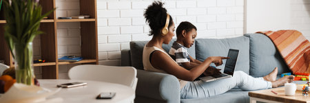 Black mother and son using laptop while sitting on sofa at homeの写真素材