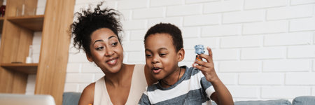 Black happy woman using laptop while playing with her son at homeの写真素材
