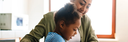 Black smiling woman drawing with her daughter at home kitchenの写真素材