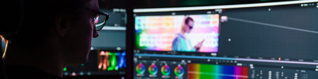 Back view of a young white man video editor sitting in front of a big screen working on a video...