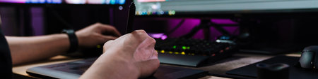 Back view of a young white man videographer working on a project with a touchpad on computer sitting...