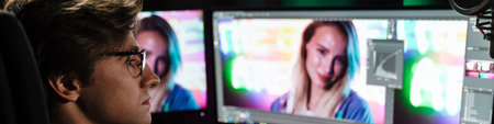 Back view of a young white man video editor sitting in front of a big screen working on a video...