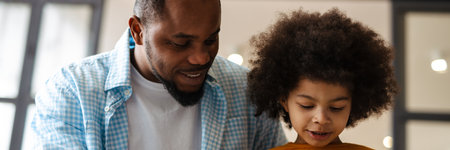 Black father and son smiling and using tablet computer while sitting on sofa at homeの写真素材
