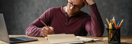The tired man resting his head with his hand while sitting at the table with papers in the studio